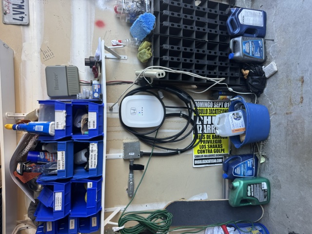 A wall-mounted EV charger with its cable coiled above blue storage bins in a garage