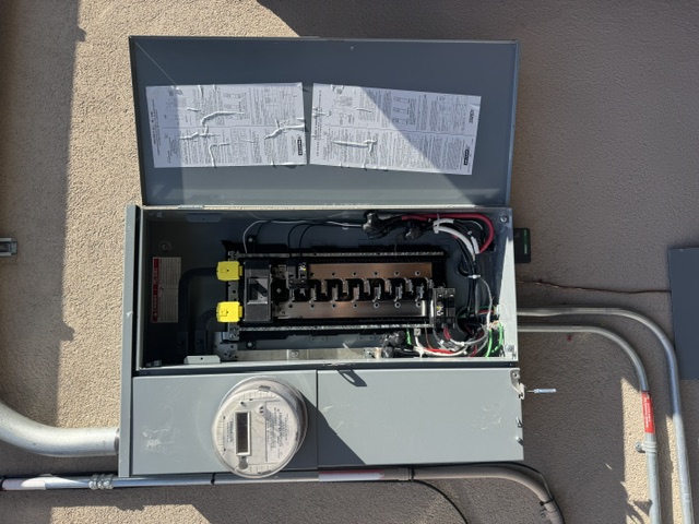 An open main electrical panel with labeled breakers and a utility meter on a stucco wall