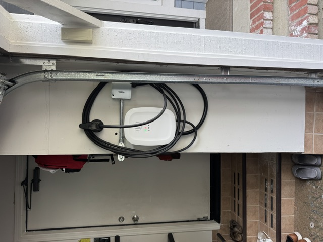 A wall-mounted EV charger with its cable coiled on a garage wall next to a doorway