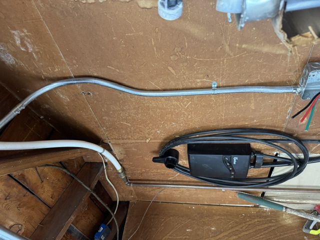 Conduit running down a garage wall to a mounted EV charger with the cable coiled beneath it