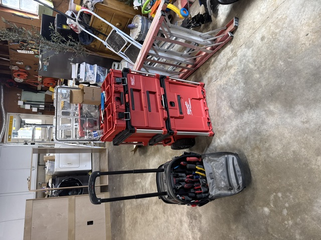 An electrician's rolling tool bag and red tool case in a garage
