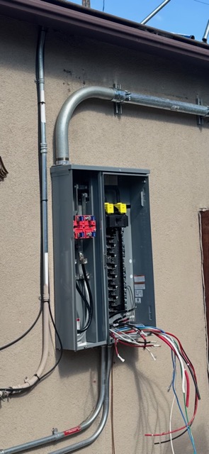 An open outdoor electrical panel with new conduit and wires being terminated