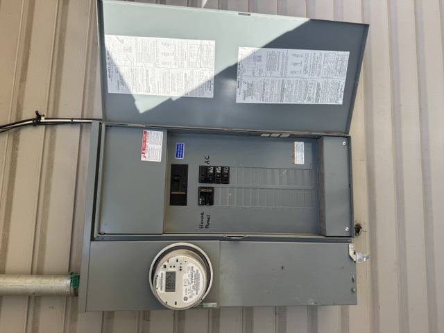 An exterior main panel with its door open, showing a utility meter and labeled breakers on vinyl siding