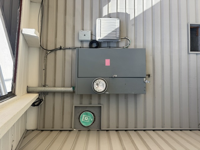 A utility meter and service disconnect on a siding wall under a roof overhang