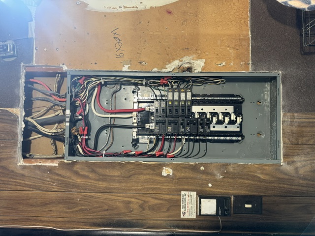 An open electrical panel with neatly dressed red and black wiring set into a wood wall