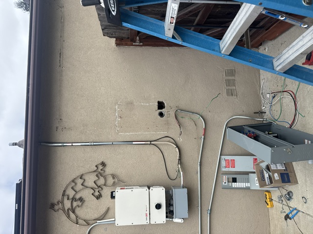 A blue ladder beside a solar inverter, conduit and a new panel on a stucco wall