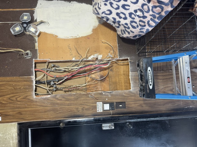 A wall cavity with cables pulled out ahead of a panel replacement, with a blue ladder in front