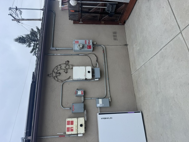 An exterior wall with a solar inverter, disconnect switches and a wall-mounted battery unit
