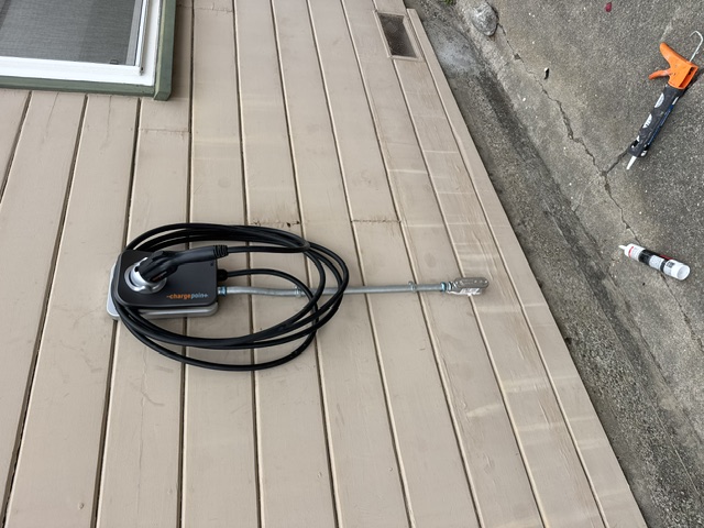 A black EV charger cable coiled on a wall-mounted charger on tan lap siding