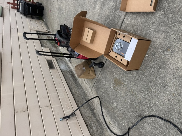 An EV charger box being unpacked on the ground below a meter box on siding